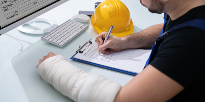 Injured worker with a cast on his arm filling out paperwork, alongside a yellow hard