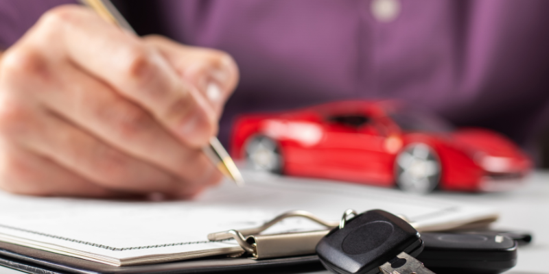 Person writing notes with a pen, a car key, and a small red toy car