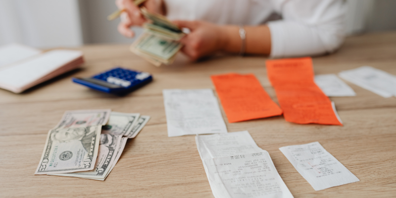 Person counting cash and organizing receipts on a wooden table, illustrating financial management strategies for