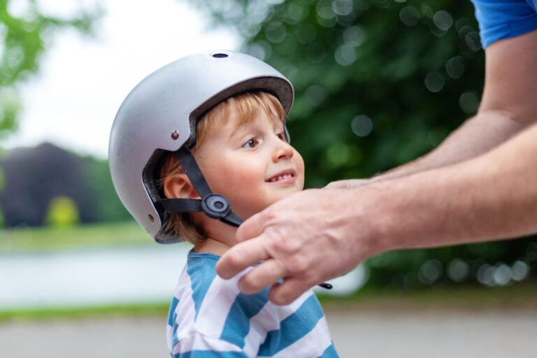 Child wearing a bicycle helmet while an adult adjusts it, emphasizing safety and brain injury