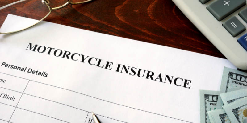 Motorcycle insurance form on a wooden table with a calculator and cash, representing financial considerations