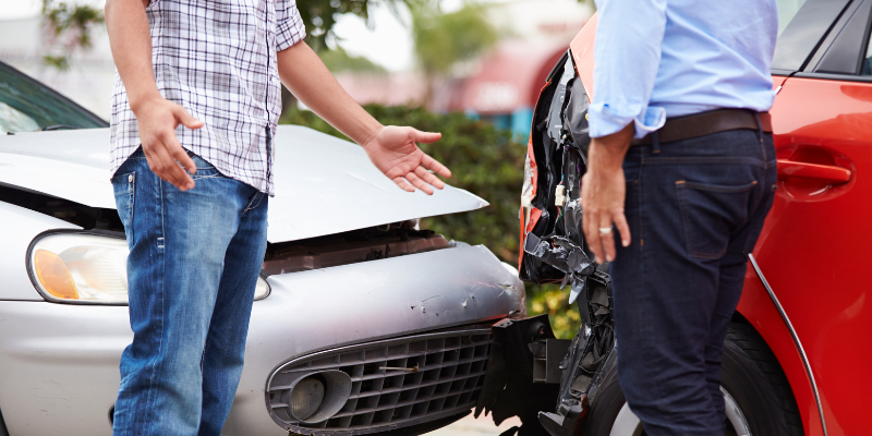 Two men discussing a car accident, with one gesturing towards the damaged vehicles, emphasizing the
