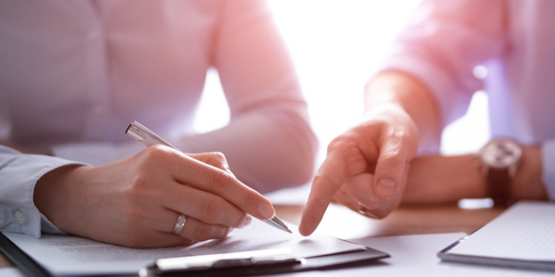 Person signing a document while another points to it, illustrating the legal consultation process for