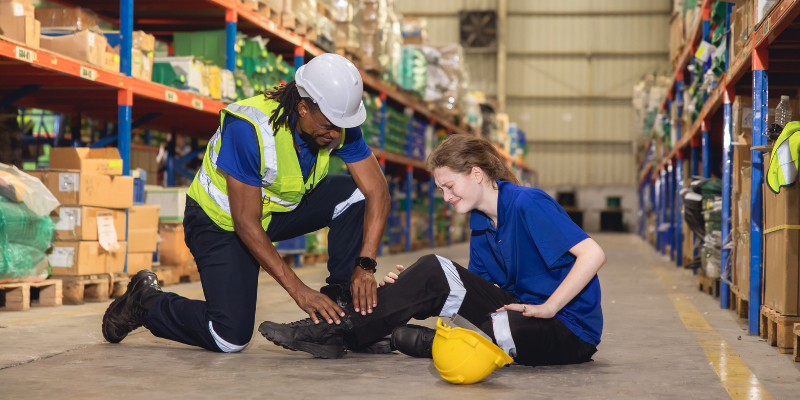Worker assisting an injured colleague in a warehouse, highlighting the importance of workplace safety and