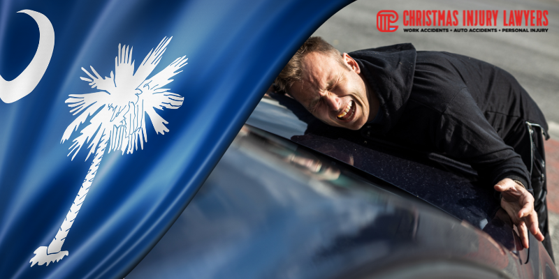 A distressed man leaning on a car, with the South Carolina flag in the background,
